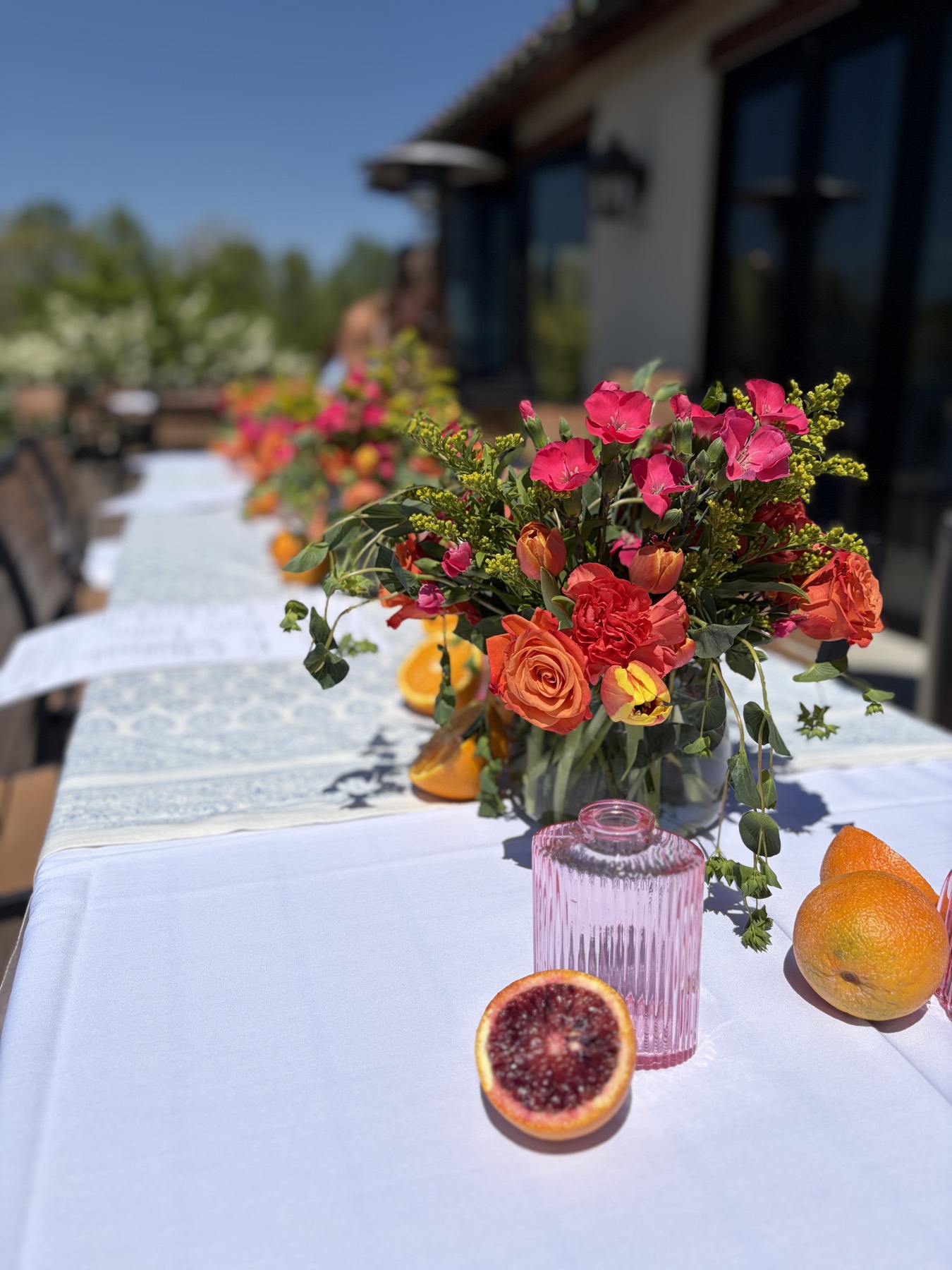 Outdoor long table with orange and coral floral arrangements