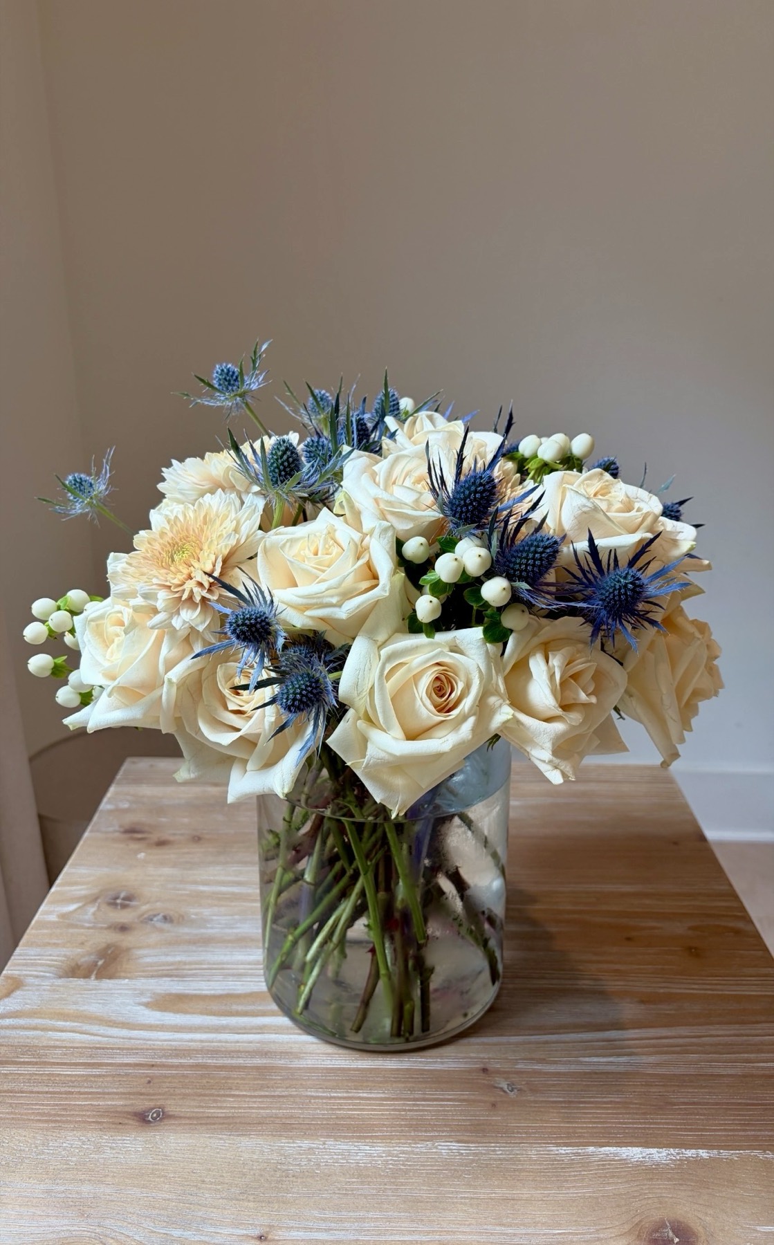 Cream roses, dahlia and blue thistle arrangement in a glass vase