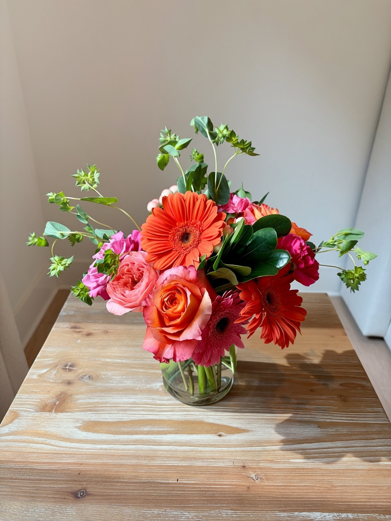 Coral gerbera, roses and hot pink bouquet in a glass vase