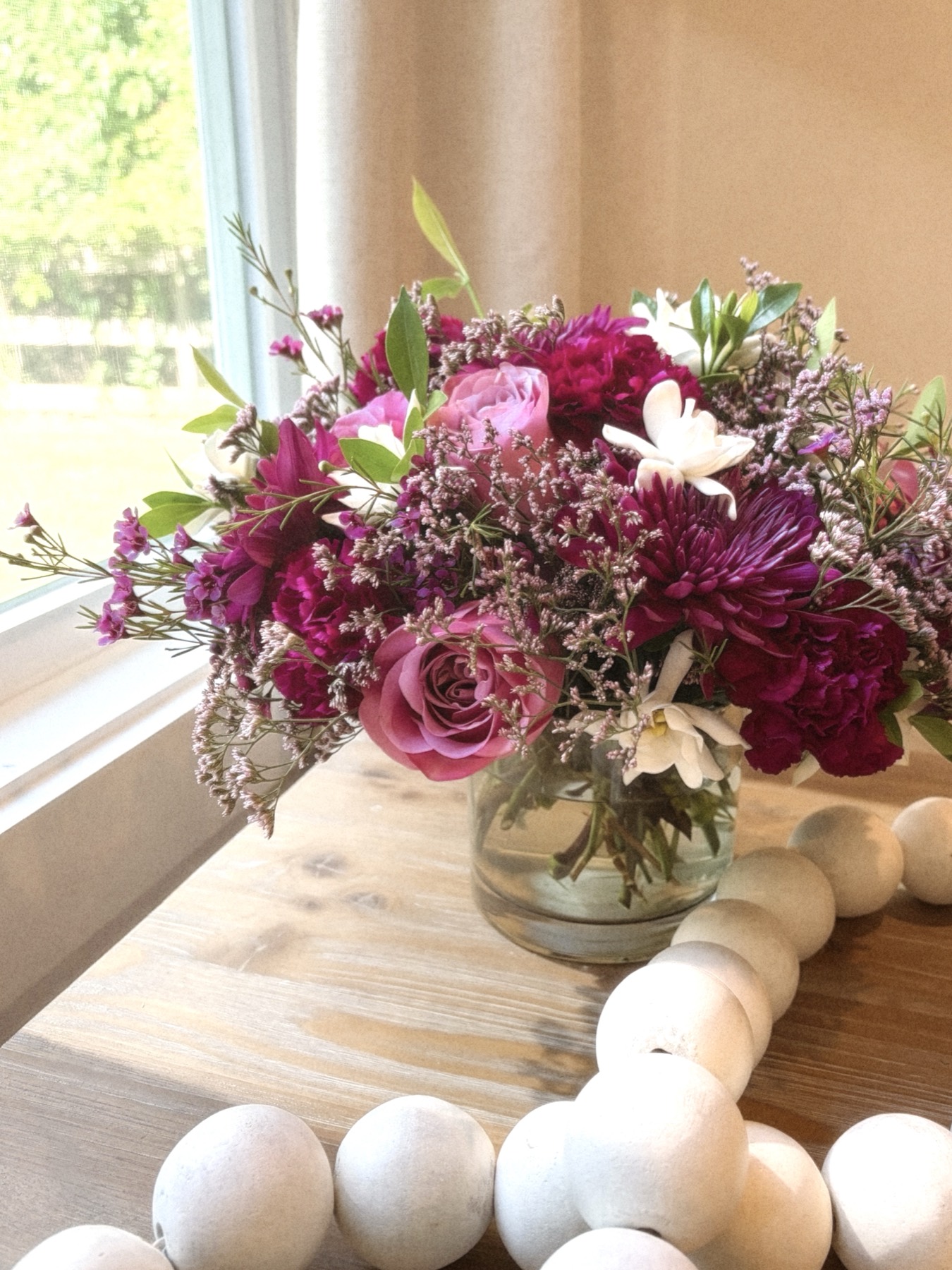 Berry-toned bouquet with magenta roses, pink garden roses and white narcissus by a window