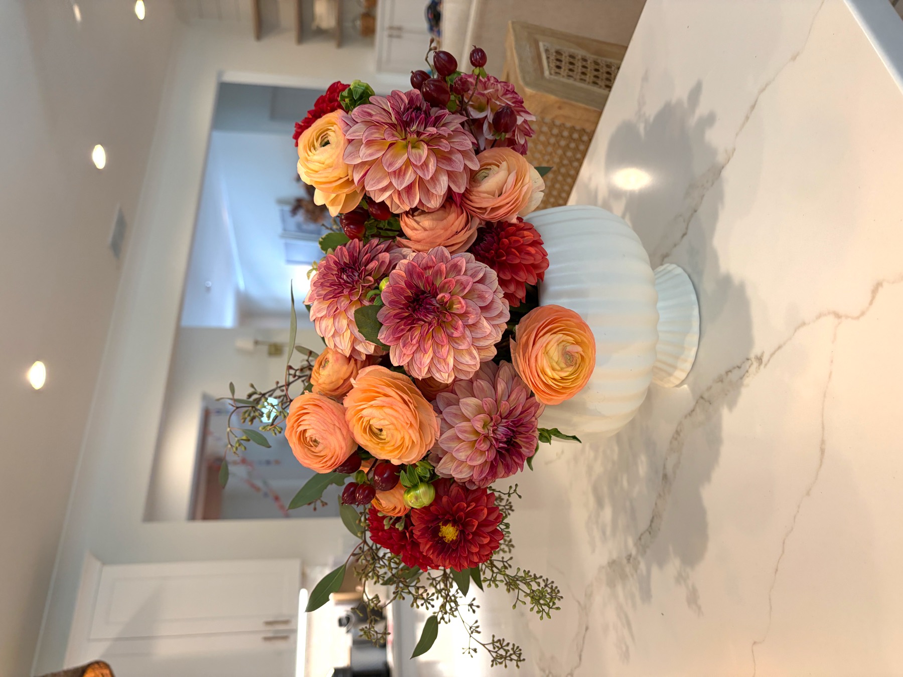 Autumn arrangement of peach ranunculus and mauve dahlias in a white footed bowl on a marble island